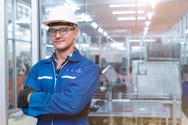 El işçisinin portresi, yüksek teknoloji temiz endüstri fabrikasının cam duvarının önünde mavi çalışma odası elbisesi ve güvenlik kaskıyla ayakta duruyor..
