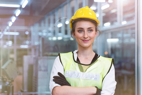 Elle çalışan kadın işçinin portresi, mavi çalışma süitiyle yüksek teknoloji temiz endüstri fabrikasının cam duvarının önündeki güvenlik elbisesi ve miğfer için kendinden emin bir şekilde duruyor..