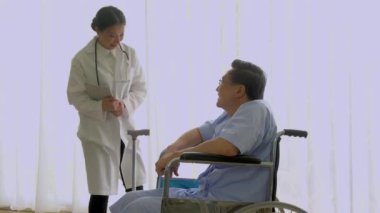 Asyalı kadın doktor, yaşlı yaşlı bir hastaya tablet bilgisayarında tavsiye veriyor. Hasta odasında tekerlekli sandalyede oturuyor. Hastanedeki arka plan beyaz perde..