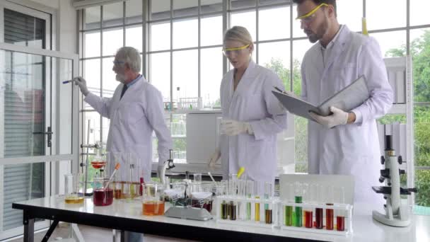 一组身穿白袍的科研人员在课桌上准备研究课题的公式模式和化学测试设备 — 图库视频影像