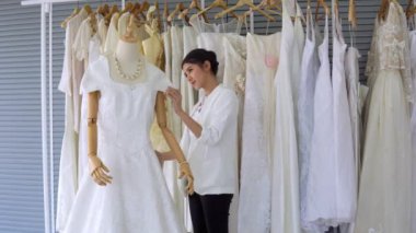 Kuaför Asyalı kadın moda gelinliği stüdyosundaki en iyi beyaz gelinliği ayarlar ve seçer. Giyim sektöründe beyaz düğünün arka planında.