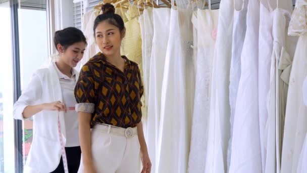 スタイリストアジアの女性が調整し ファッション布の結婚式のスタジオで最高の白いウェディングドレスを選択します 白い結婚式の背景を持つ服のライン — ストック動画