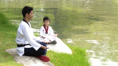 Karate spor süitindeki bir adam ve çocuk açık hava parkındaki kayada meditasyon yapıyorlar..