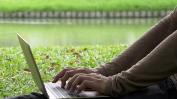 Zavřít dvě ruce muže pomocí notebooku a prsty dotek na klávesnici počítače v venkovní zelený park. — Stock video