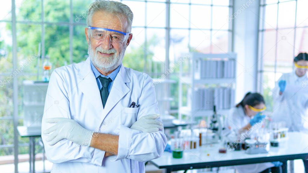 Handsome senior scientist man wearing white dress coat stand in front interior laboratory background smiling positive. Successful face and feeling expression.