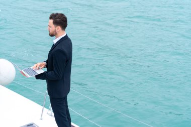 Deniz ve beyaz gökyüzü geçmişine sahip deniz yatında akıllı telefonları olan bir iş adamı. İş seyahati kavramı.