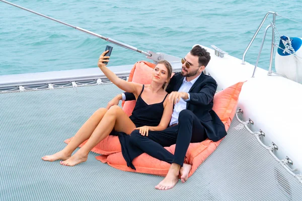 luxury relaxing couple traveler in nice dress and suite sit on bean bag and drink a glass of wine in part of cruise yacht with background of sea and white sky. Concept business travel.
