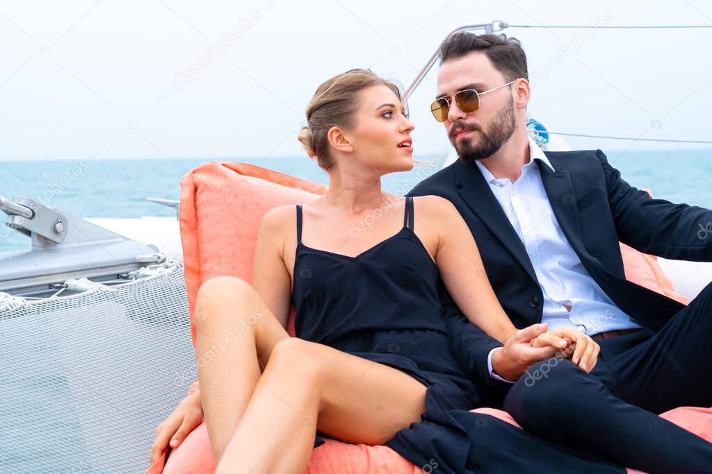 luxury relaxing couple traveler in nice dress and suite sit on bean bag in part of cruise yacht with background of sea and white sky. Concept business travel.