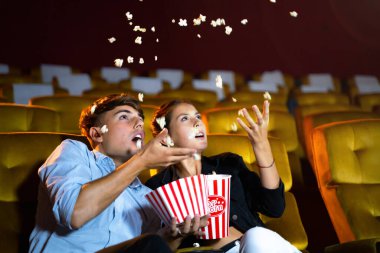 Film izleyen genç çiftler sinemada kendilerini korkutucu ve korkutucu hissediyorlar. Elinde çerez kovası ve koltuğun etrafına patlamış mısır at..