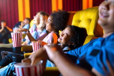 Kız ve bir grup çocuk sinema koltuklarında oturup film izliyorlar. Yüzler mutlu ve keyiflidir..