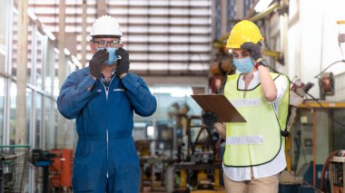 Makine endüstriyel fabrikasında güvenlik için maske takan bir grup işçi fabrikası ve depo makinelerini kontrol ediyorlar..