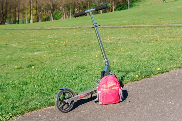 Scooter ve yeşil çayır yanında sırt çantası.