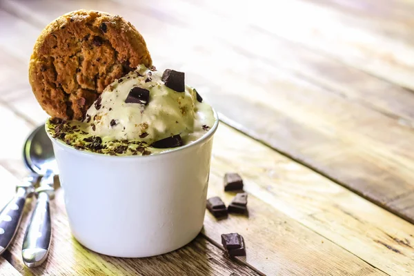 Ceramic bowl of banana ice cream dessert with chocolate and cookies, close-up on wooden background with copy space. Selective focus