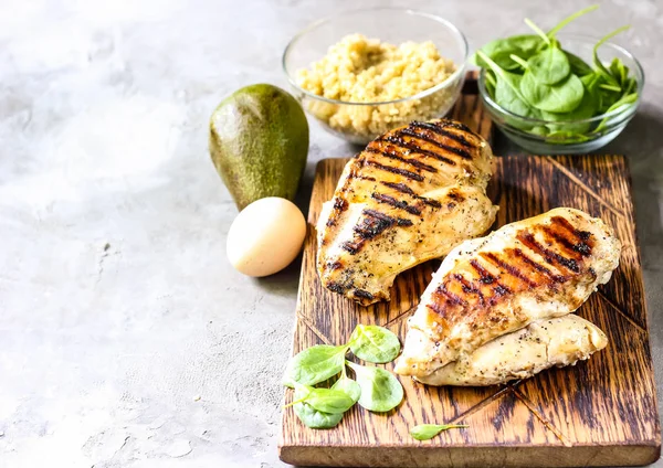 grilled chicken fillets on wooden cutting board prep with cooked quinoa and spinach for healthy food