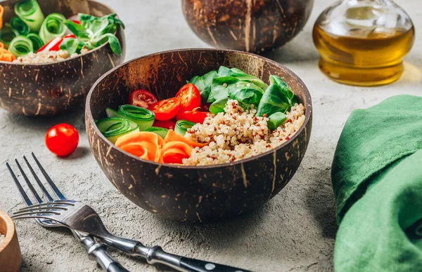 Vegan Buddha bowl. Healthy meal quinoa, tomato, cucumber, carrot, radish, corn salad in coconut bowls on concrete background. Selective focus