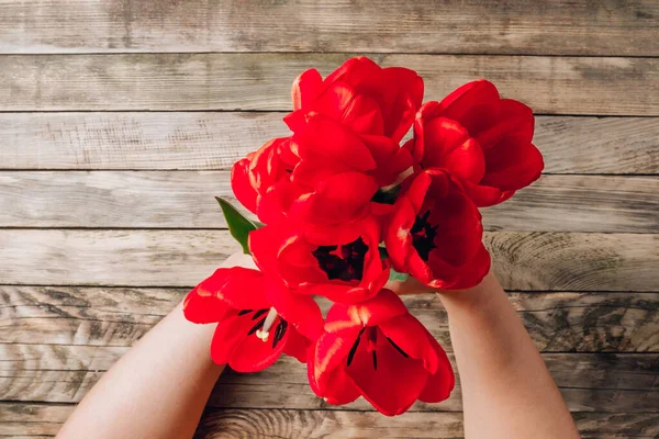 Tulip bouquet in female hands on rustic background. Flat lay, top view