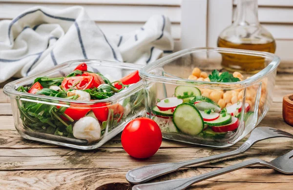 Healthy meal prep containers with chickpeas and spring salad with cucumbers, radish and chives and containers with caprese salad with arugula. Healthy lunch in glass containers. Zero waste concept.