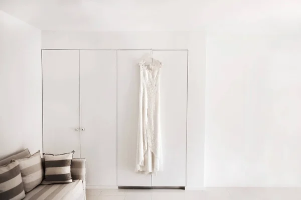 Wedding dress hanging on the wall in the white room — Stock Photo, Image
