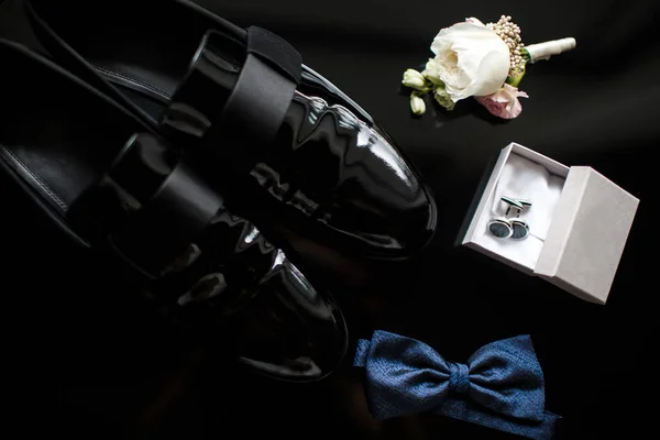 Close up of modern man accessories. Blue bowtie, black shoes, boutonniere and cufflinks
