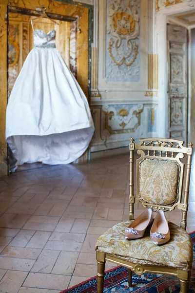 Hochzeitskleid hängt im Zimmer und Schuhe auf einem Vintage-Stuhl — Stockfoto