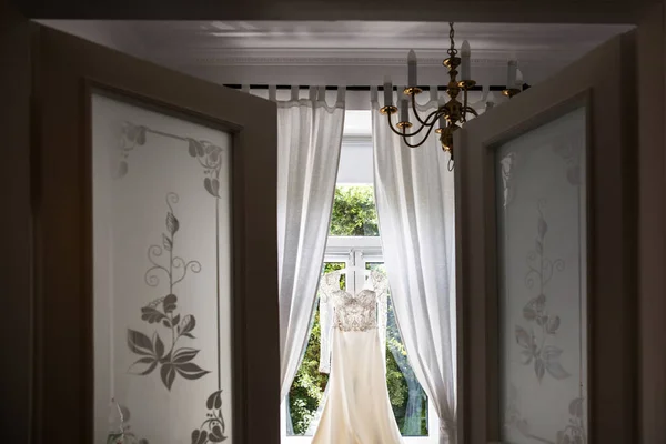Wedding dress hanging on the window in the room — Stock Photo, Image