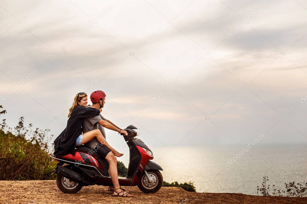 lovers on a scooter on a cliff near the sea against a sunset background