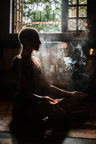 キャンドルから煙の窓から太陽の光の瞑想のポーズの女の子 — ストック写真