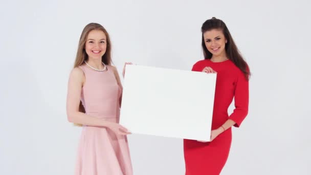 Duas garotas atraentes sorridentes segurando um banner branco em branco — Vídeo de Stock