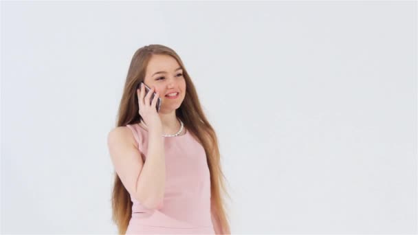 Улыбающаяся привлекательная девушка в розовом платье разговаривает по телефону, глядя налево и вверх — стоковое видео
