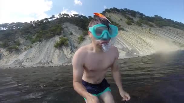 A young man on the shore of the Black Sea in a swimming mask with a tube jumps submerges under the water. Summer fun, water sports. Coast of the Black Sea. Spray from immersion. Go-Pro video camera. — Stock Video
