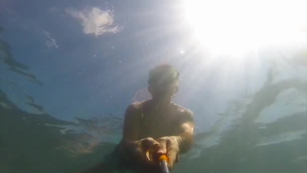 Ein junger Mann mit Schwimmmaske und Schlauch schwimmt in der Sonne unter dem Wasser. — Stockvideo