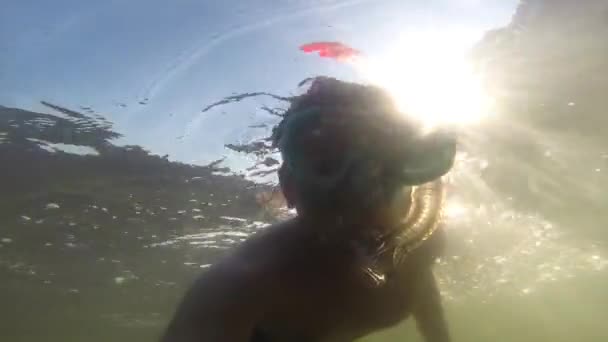 Un joven flotando bajo el agua en una máscara con un tubo está flotando en el sol . — Vídeo de stock