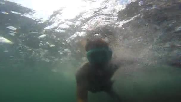 A young man under the sea in a mask and a tube floats and waves his hands creating bubbles. — Stock Video