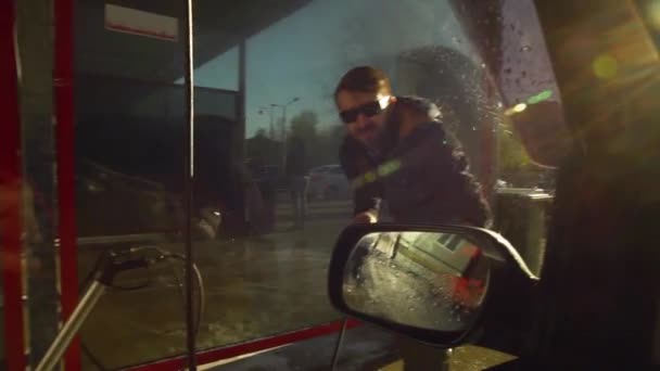 Молодий чоловік в окулярах миє склянку своєї машини в автомийці самообслуговування з автомобіля — стокове відео