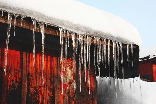 Icicle and snow on the roof. Cold season. Snowdrift and icicle on the roof of a country wooden house in the winter.