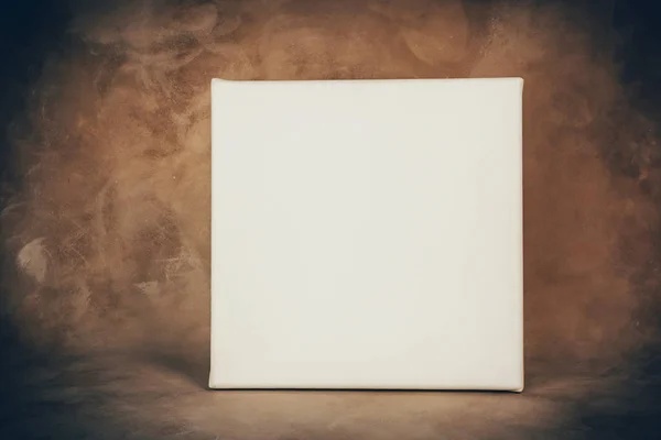 Square blank canvas board on brown art backdrop.