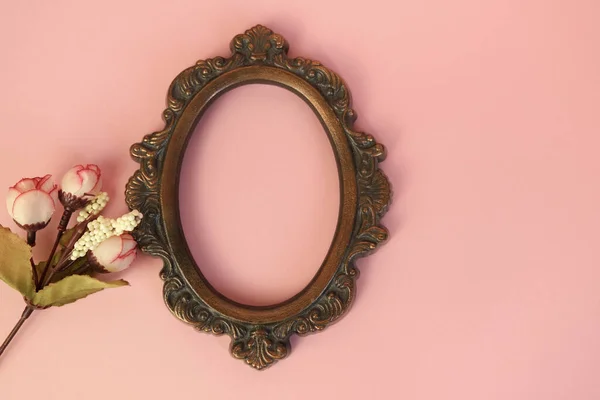 Oval vintage picture frame and flowers on pink background. Home decor, empty photo frame.