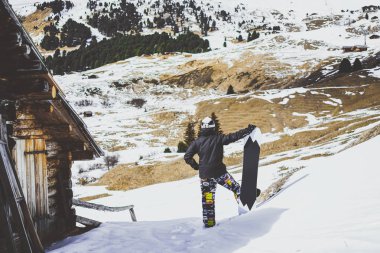 Üzerinde siyah ceket, maske ile snowboard snowboard otantik ahşap ev kapatın. Panoramik mountans manzaraya bakacak adam. Yatay.