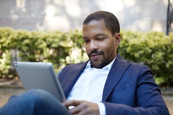 Ung amerikansk afrikanska affärsman i informella kläder arbetar på soliga gatan på elektronisk Touchpad, kontrollera e-post med hjälp av Internet-aktiverad elektronisk enhet, ringa vänner via sociala nätverk. — Stockfoto