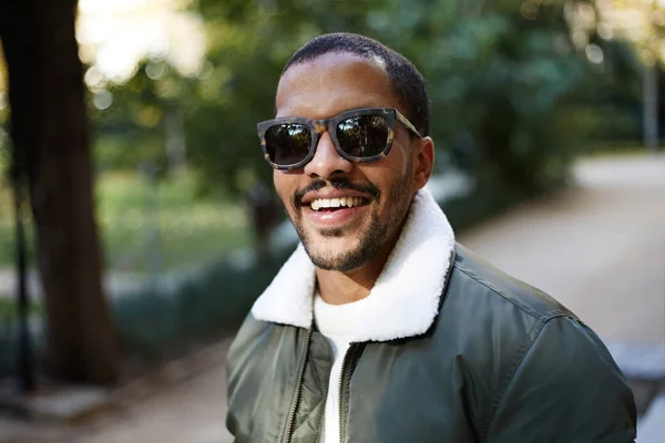 Портрет счастливого молодого афро-американского хипстера в официальной одежде и солнцезащитных очках, сидящего в городском парке. . — стоковое фото