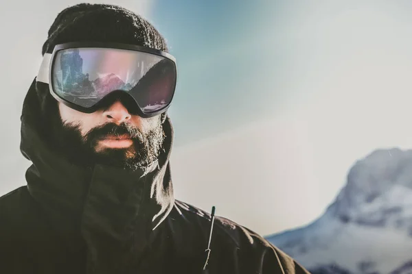 Retrato de joven barbudo snowboard en máscara de gafas de sol, en la estación de esquí en el fondo de las montañas y el cielo azul.Fondo borroso.Imagen horizontal —  Fotos de Stock