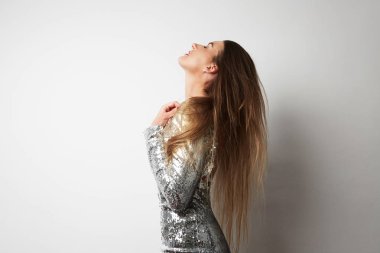 Gümüş elbise ve beyaz boş studio geçmiş vasıl poz yakın çekim sevimli genç güzel kadın. Uzay kopyalayın. Yatay. Yan görünüm.