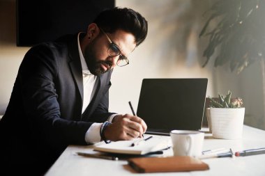 Genç salon evde çalışan erkeğin sakallı. Not yazmak ve Elektronik Gadget'ı kullanarak bir adam. Arka plan bulanık