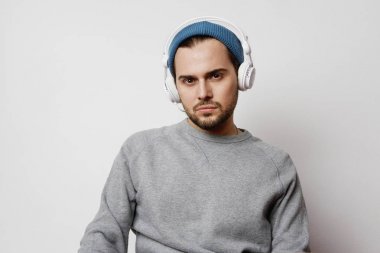 Stüdyoda boş açık renkli üzerinde kulaklık müzik dinlemek dalgın genç adam. Yatay.