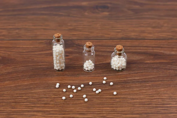 Homeopathic globules and three glass bottles on wooden background