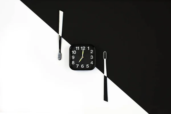 Beyaz ve siyah arkaplana elle diş fırçası takılmış siyah alarm saati. — Stok fotoğraf