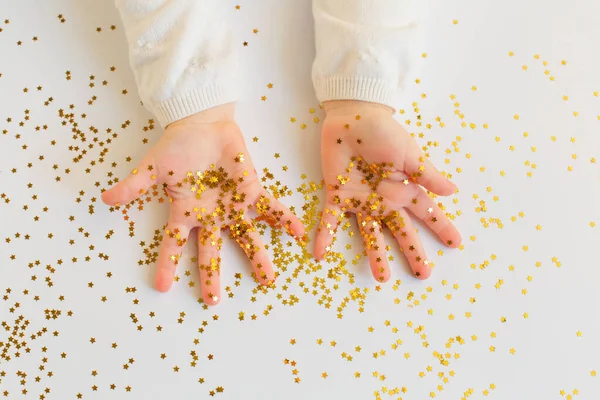 Bebé jugar con estrellas de oro espolvorea en backgound luz . — Foto de Stock