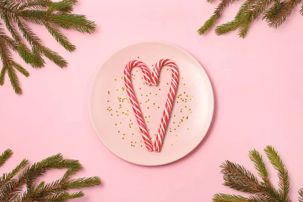 Dos bastones de caramelo en forma de corazón en estrellas de brillo de oro en placa rosa sobre fondo claro . —  Fotos de Stock