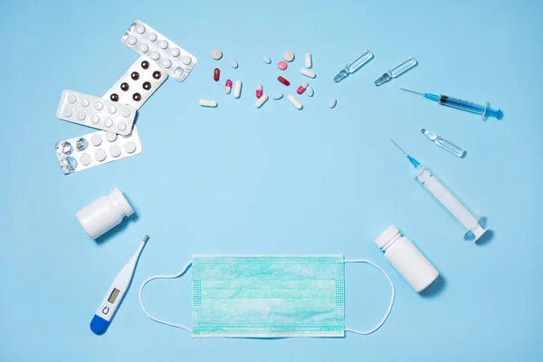 Медичні таблетки та капсули в пачках, інжекторний шприц на синьому фоні — стокове фото