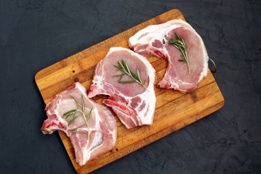 Kesme tahtasında çiğ domuz eti ve siyah arka planda baharatlar. Taze et. Üst görünüm